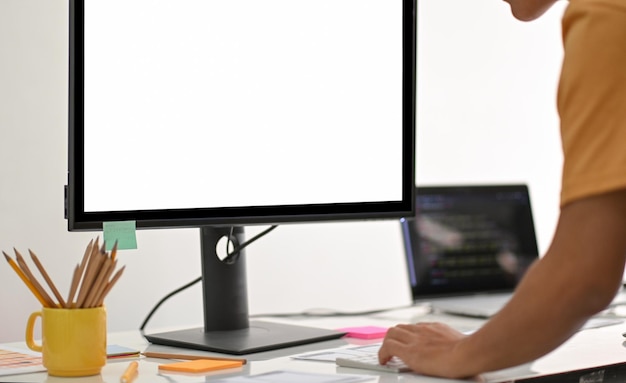 Foto een jonge man die staat en een computer gebruikt met een leeg scherm op een witte tafel