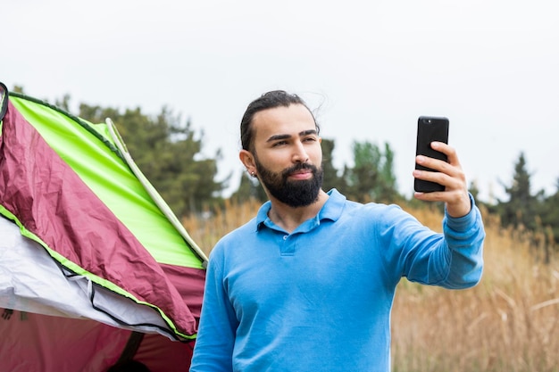 Een jonge man die voor zijn tent staat en selfie maakt