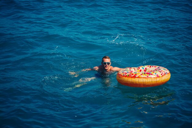 Een jonge man drijft op een opblaasbare luchtring in de zee met blauw water Feestelijke vakantie op een gelukkige zonnige dag