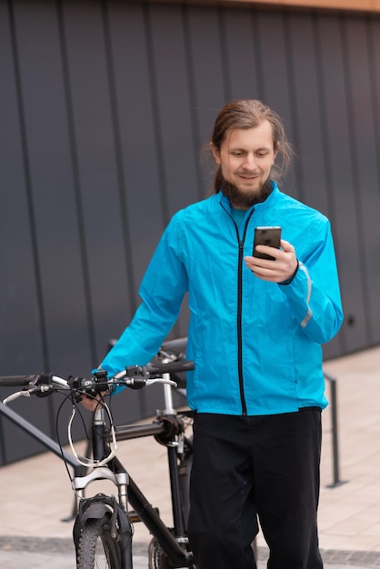 Een jonge man duwt zijn fiets en gebruikt een smartphone