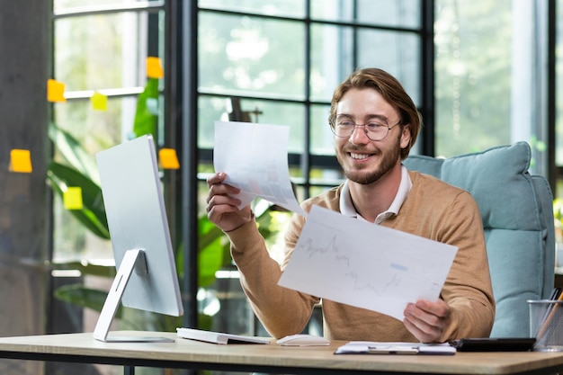 Een jonge man, een zakenman, een programmeur zit op kantoor achter een computer en werkt met documenten