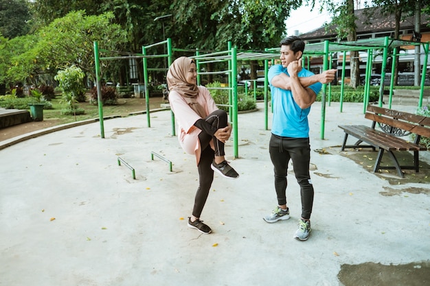 Een jonge man en een meisje in een sluier chatten terwijl ze warming-up bewegingen doen voordat ze in het park gaan trainen