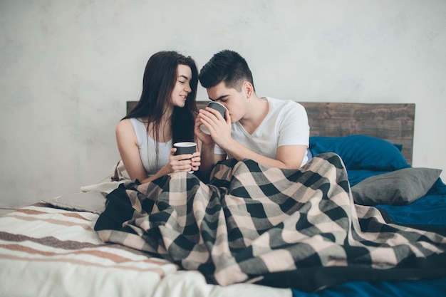 Een jonge man en een vrouw drinken 's ochtends koffie in bed. Romantische ochtend thuis