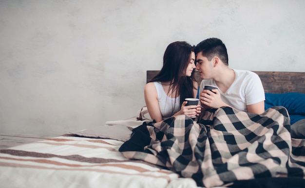 Een jonge man en een vrouw drinken 's ochtends koffie in bed. Romantische ochtend thuis