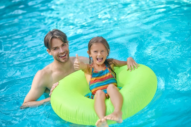 Een jonge man en zijn dochter zwemmen in het zwembad en kijken genoten