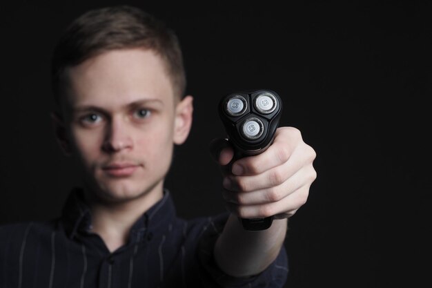 Foto een jonge man houdt een elektrisch scheermes met drijvende bladen in zijn hand foto van hoge kwaliteit