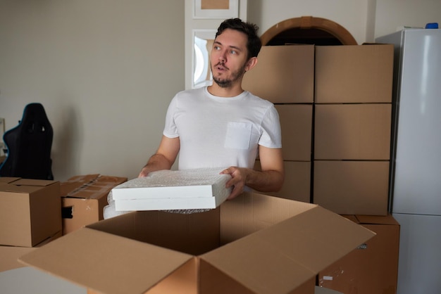 Een jonge man hurkte neer en keek door een verhuisdoos vol met kledingboeken en een fotolijst