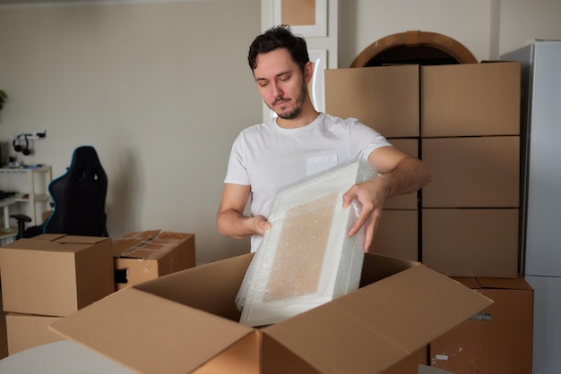 Een jonge man hurkte neer en keek door een verhuisdoos vol met kledingboeken en een fotolijst