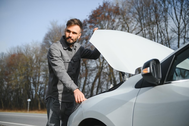 Een jonge man in de buurt van een kapotte auto met open kap langs de weg