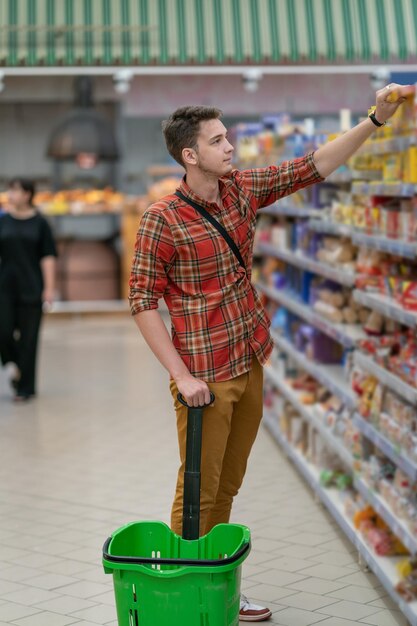 Een jonge man in een geruit overhemd doet boodschappen in een supermarkt. Een man neemt goederen van een plank