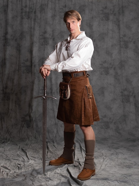 Foto een jonge man in een leren kilt en een witte blouse met veters, een schotse ridder met een zwaard met twee handen