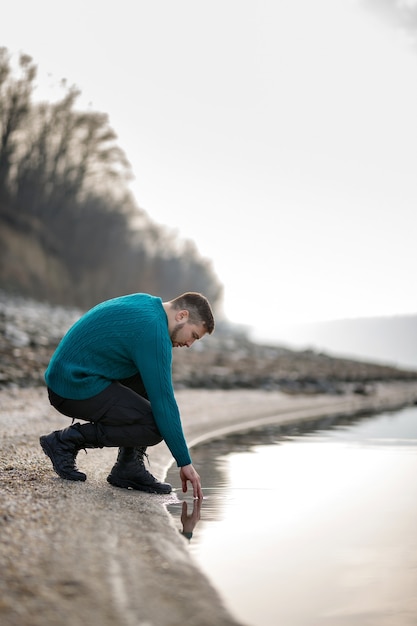Een jonge man in een turkooizen trui maakt zijn handen nat in de rivier