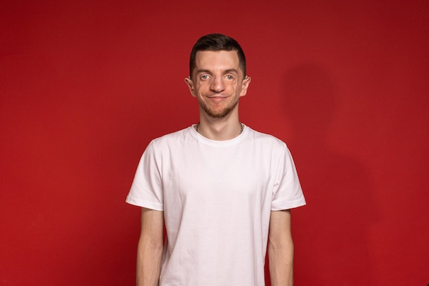 Een jonge man in een wit T-shirt staat tegen een rode achtergrond en glimlacht
