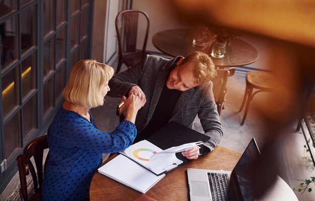Een jonge man in formele kleren heeft een zakelijk gesprek met een oude vrouw in een café.