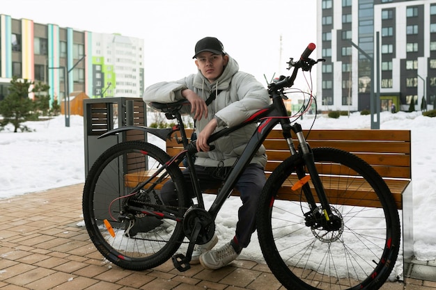 Een jonge man in herfstkleding wacht op een vriend met een fiets op straat