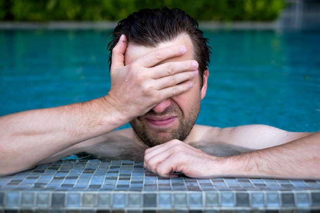 Een jonge man in het zwembad veegt zijn gezicht af met zijn hand