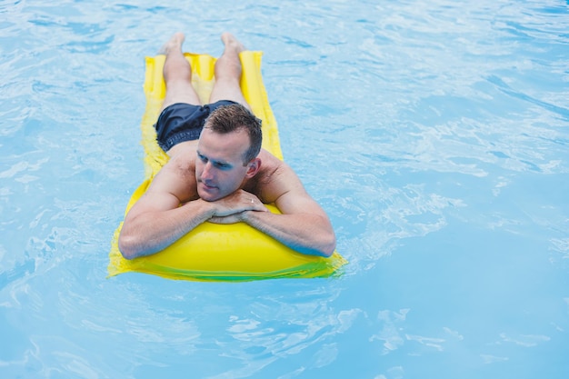 Een jonge man in korte broek geniet van het waterpark drijvend in een opblaasbare grote ring op een sprankelend blauw zwembad glimlachend naar de camera Zomervakantie