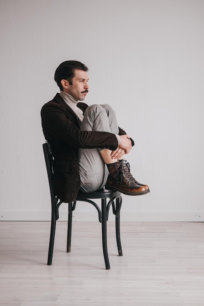 Een jonge man in spijkerbroek en jas poseert tegen een witte muur in de studio