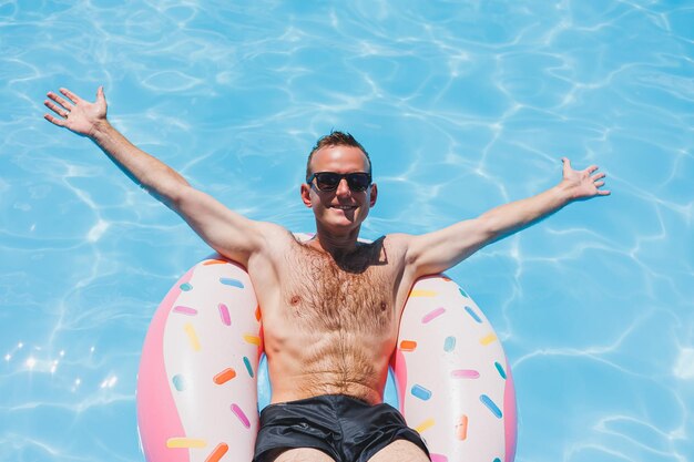 Een jonge man in zonnebril en korte broek is ontspannen op een opblaasbare donut in het zwembad Zomervakantie