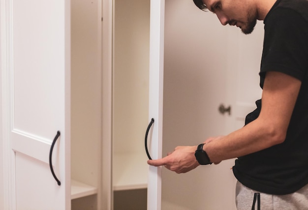 Een jonge man installeert handgrepen op de witte kastdeuren