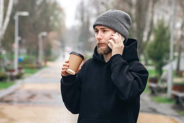 Een jonge man is aan de telefoon en drinkt koffie uit een papieren bekertje