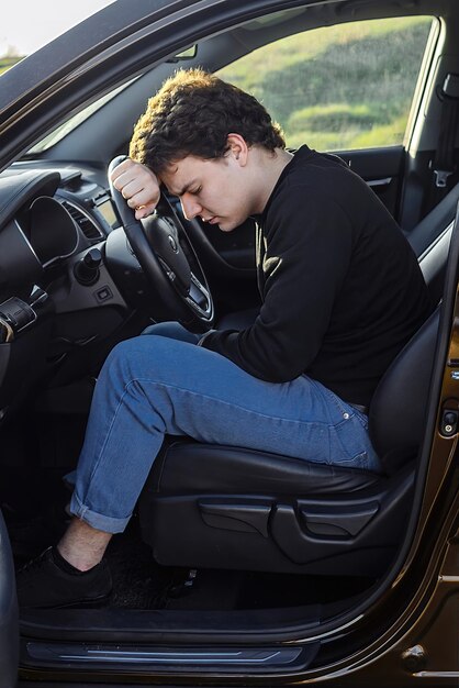 een jonge man is moe op de weg en slaapt aan het stuur van een auto
