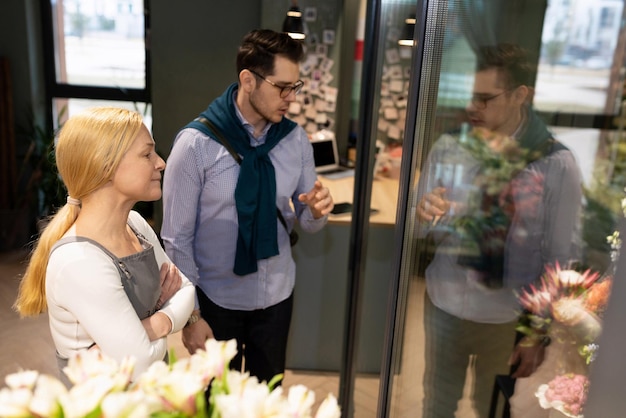 Een jonge man kiest bloemen in de koelkast naast de manager van een boekettensalon