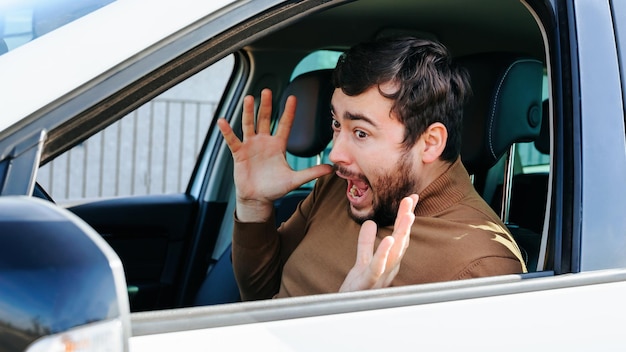 Een jonge man kijkt in de zijspiegel van zijn auto, laat het stuur los en schreeuwt