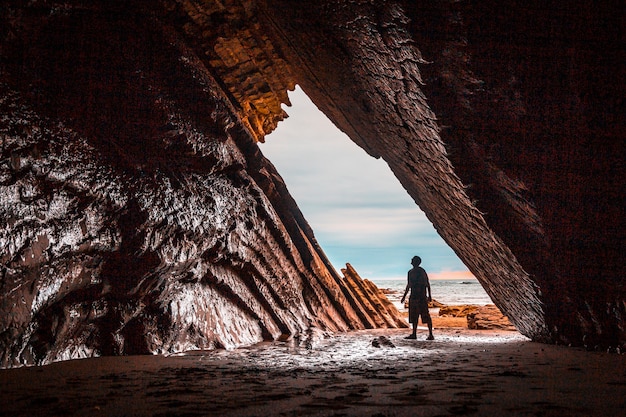 Een jonge man kijkt naar de prachtige natuurlijke grot die werd gebruikt bij het filmen van Game of Thrones in de flysch van het Itzurun-strand in Zumaia.