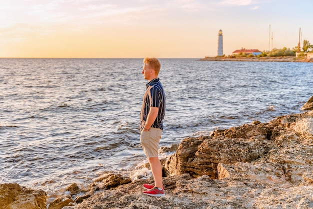 Een jonge man kijkt naar de zonsondergang op de zee en de vuurtoren Krim Prachtige zee kleurrijk