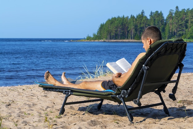 Een jonge man leest een boek op een chaise longue op een zandstrand