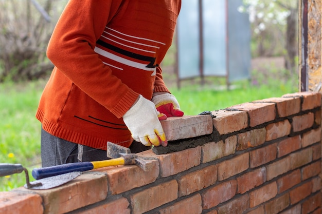 Een jonge man legt een baksteen op cementmortel