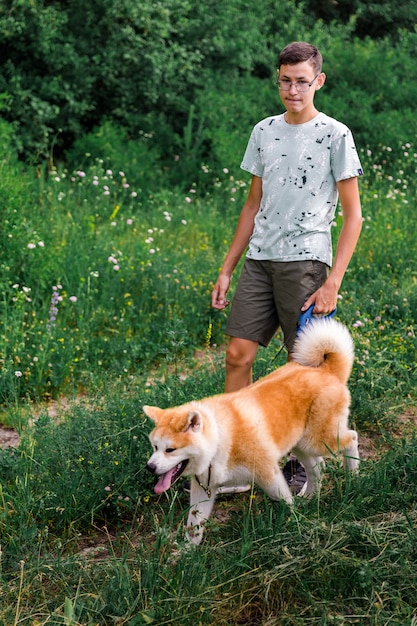 een jonge man loopt in een zomerpark met een jonge puppy van het akita-ras