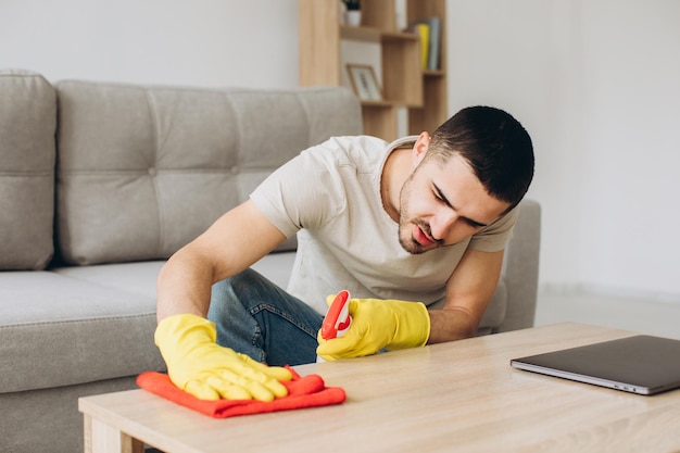 Een jonge man maakt thuis de woonkamer schoon, veegt de tafel af