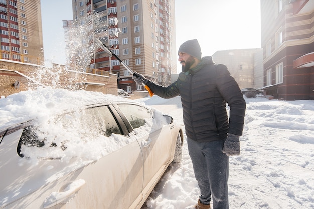 Een jonge man maakt zijn auto schoon na een sneeuwval op een zonnige, ijzige dag.