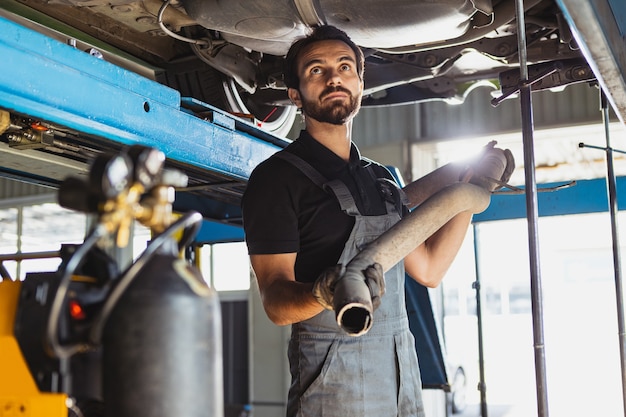 Een jonge man, mannelijke automonteur in tuinbroek die bij de autoservice werkt