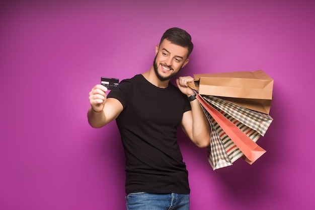 Een jonge man met boodschappentassen en creditcard in handen poseren geïsoleerd op violet