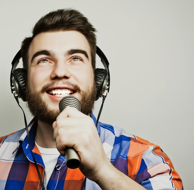 Een jonge man met een baard draagt een shirt met een microfoon en zingt, hipsterstyle.Over grijze achtergrond.