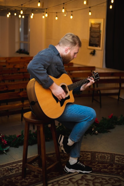 Een jonge man met een baard speelt een akoestische gitaar in een kamer met warme verlichting