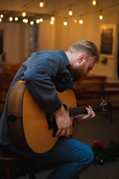 Een jonge man met een baard speelt een akoestische gitaar in een kamer met warme verlichting