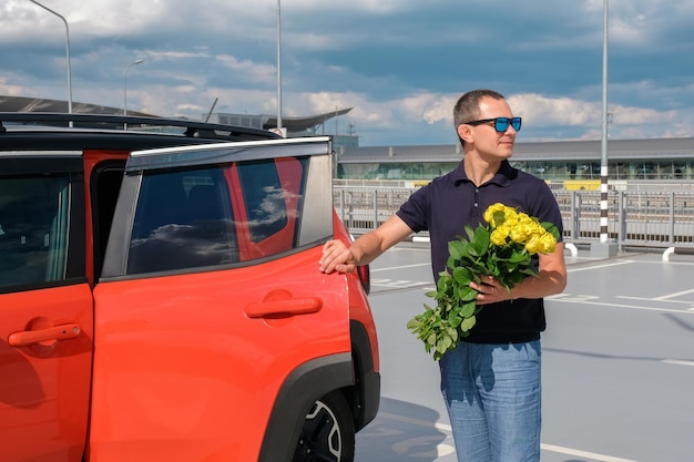Een jonge man met een boeket bloemen staat in de buurt van zijn auto in een stadsstraat