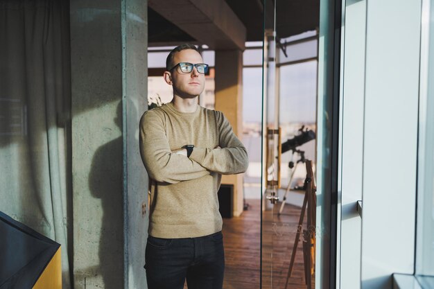 Een jonge man met een bril en vrijetijdskleding staat in een moderne werkruimte Mannelijke freelancer werkt op afstand