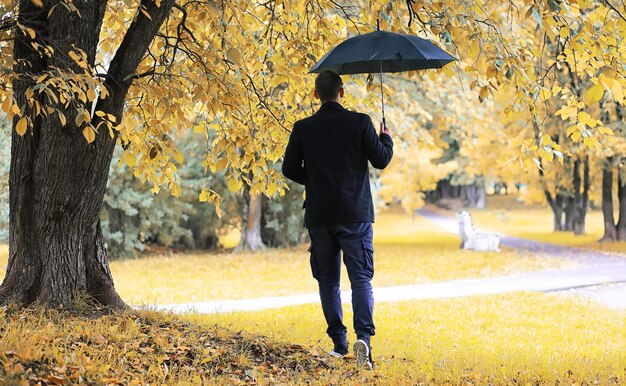 Een jonge man met een bril loopt in het park met een paraplu tijdens de regen.