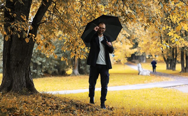 Een jonge man met een bril loopt in het park met een paraplu tijdens de regen.