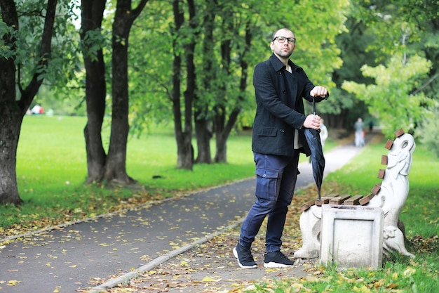 Een jonge man met een bril loopt in het park met een paraplu tijdens de regen.