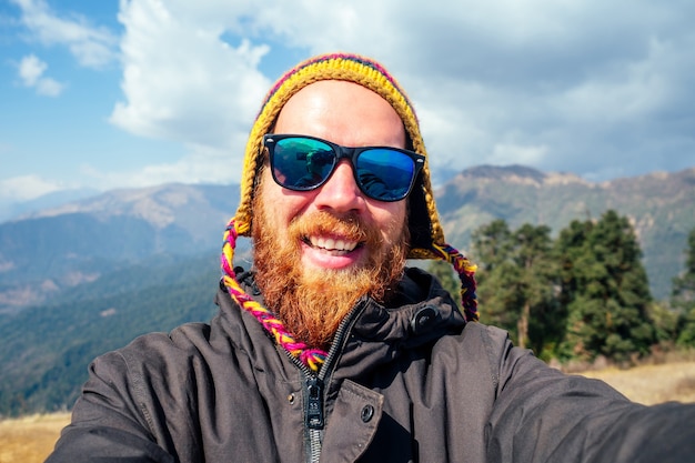 Een jonge man met een rode baard en een rugzak in de bergen maakt een selfie. het concept van actieve recreatie en toerisme in de bergen. Nepal in de lente.