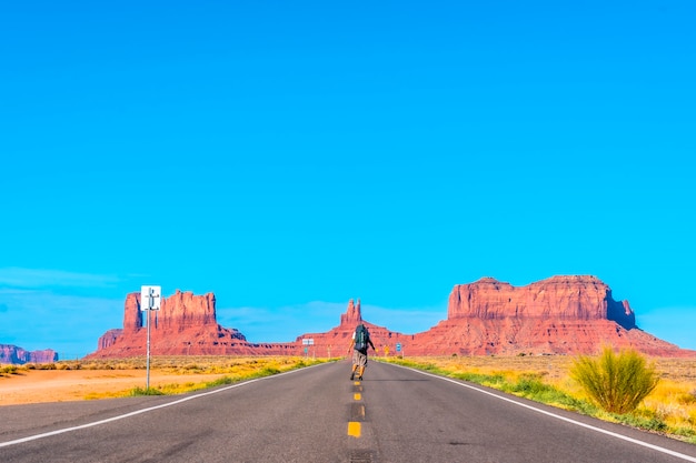 Een jonge man met een wit t-shirt en een groene rugzak op de weg van Monument Valley. Utah