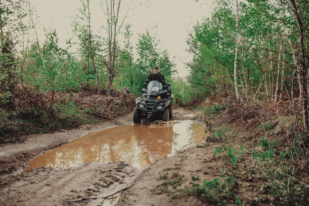 Een jonge man met een witte helm rijdt door het bos op een quad Extreme hobby Een reis naar ATV op de weg van boomstammen Quad Biking door het bos