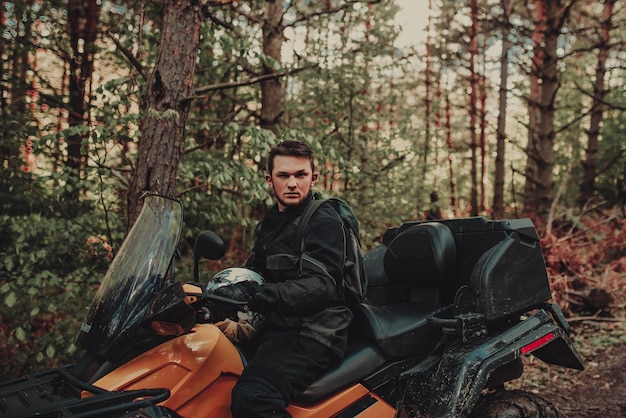 Een jonge man met een witte helm rijdt door het bos op een quad Extreme hobby Een reis naar ATV op de weg van boomstammen Quad Biking door het bos