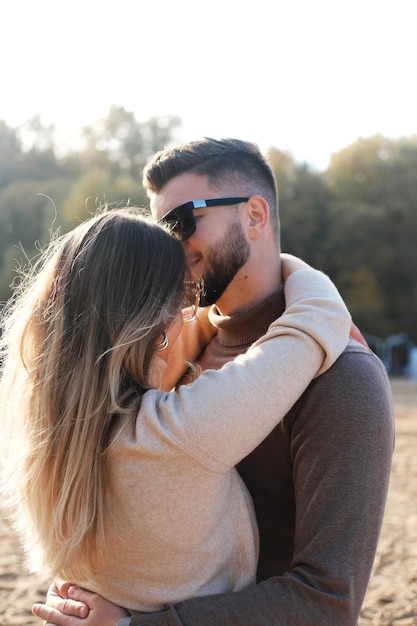 Een jonge man met een zwarte zonnebril omhelst een meisje bij haar middel en kust haar op het voorhoofd